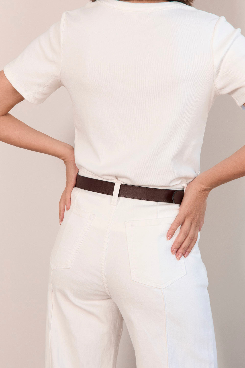 Person wearing a white shirt and white pants with a brown belt on a plain background