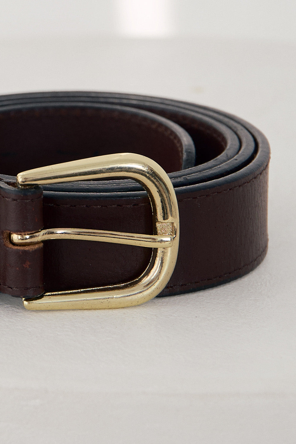 Brown leather belt with a gold buckle on a light gray background