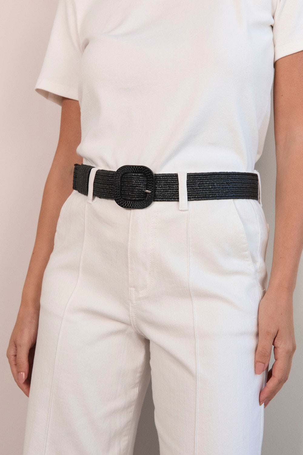 Person wearing a black belt with a white shirt and light-colored pants on a plain background