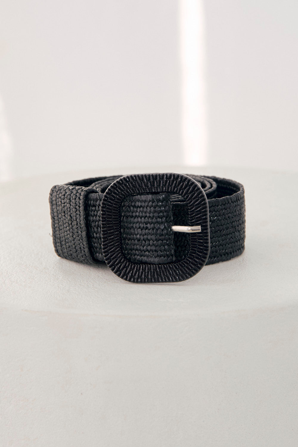 Black woven belt with a silver buckle on a light gray background