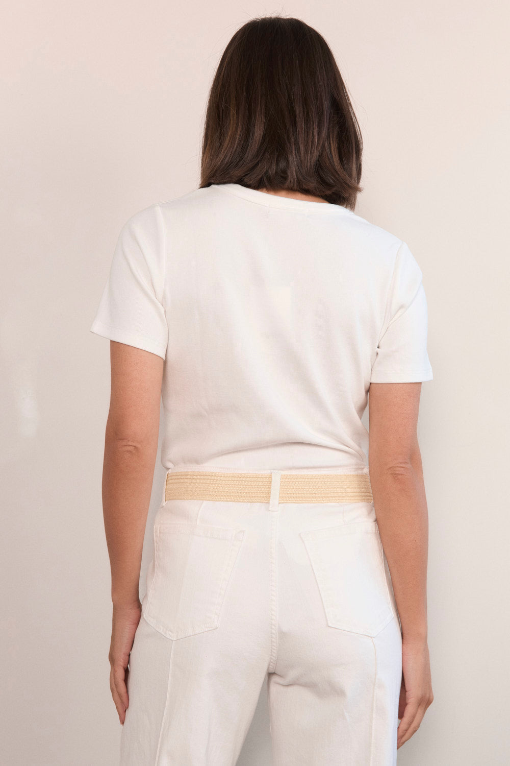 Person wearing a white t-shirt and pants with a beige belt against a plain background