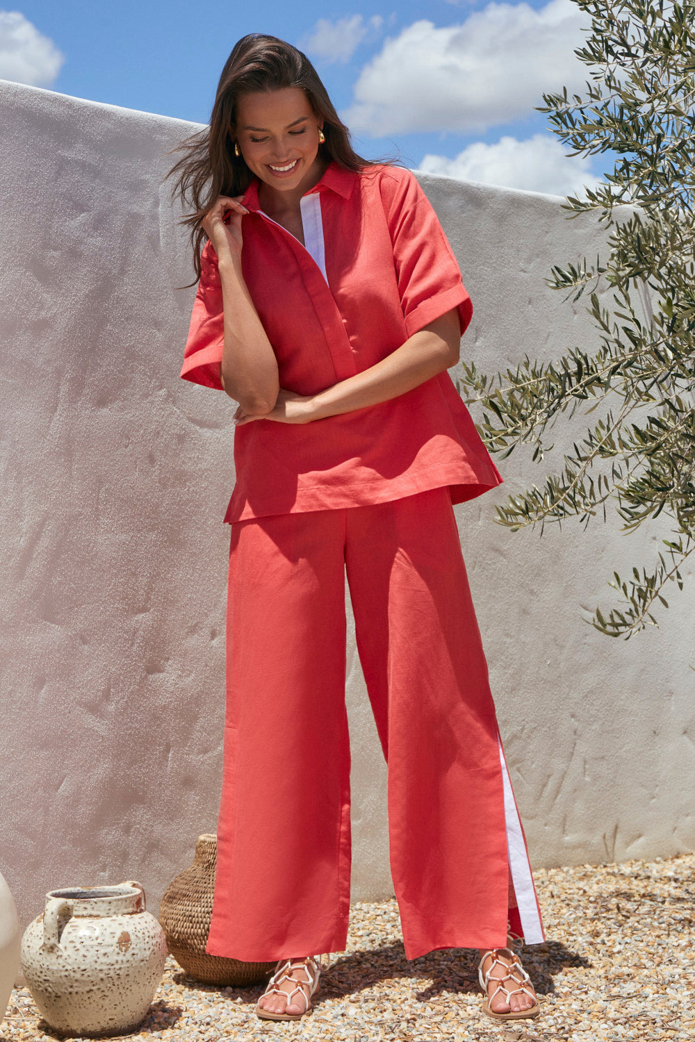 Woman in a coral outfit standing outdoors with a neutral wall and plant in the background