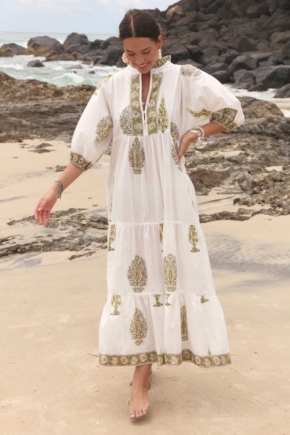 Woman in a white embroidered dress standing on a rocky beach.