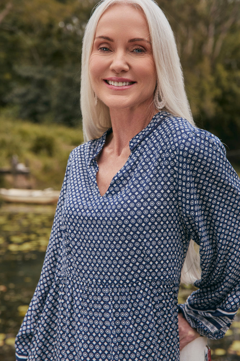 Woman wearing a blue patterned shirt outdoors with greenery in the background