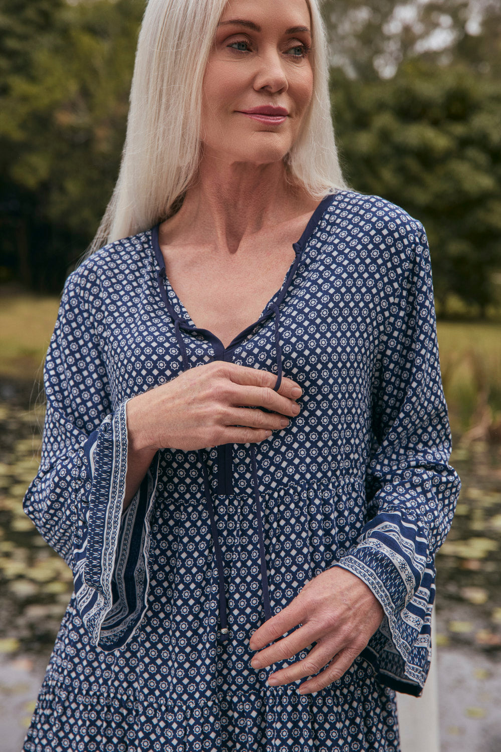 Woman wearing a blue patterned dress outdoors with greenery in the background