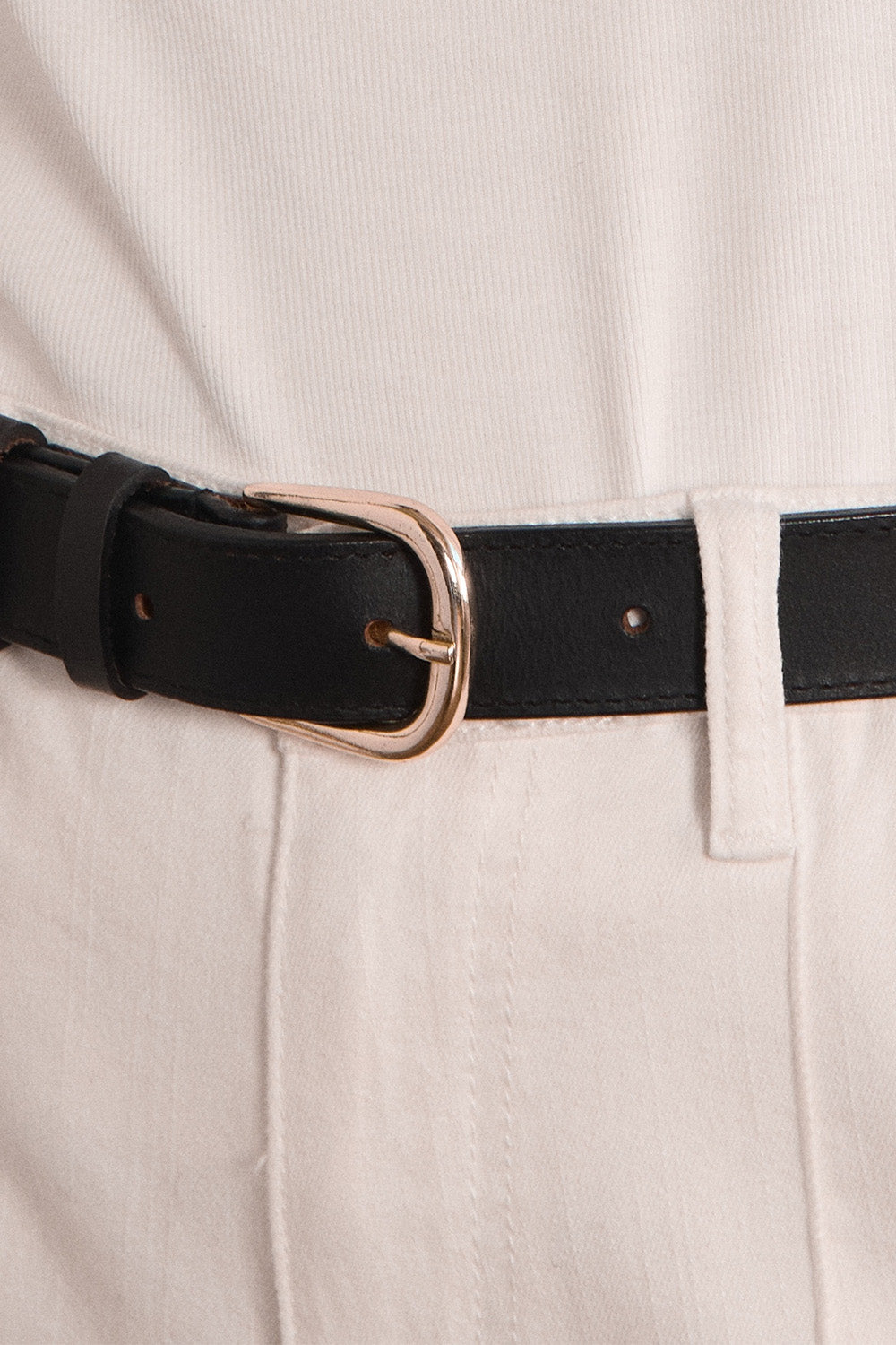Close-up of a black belt with a rose gold buckle on beige pants.