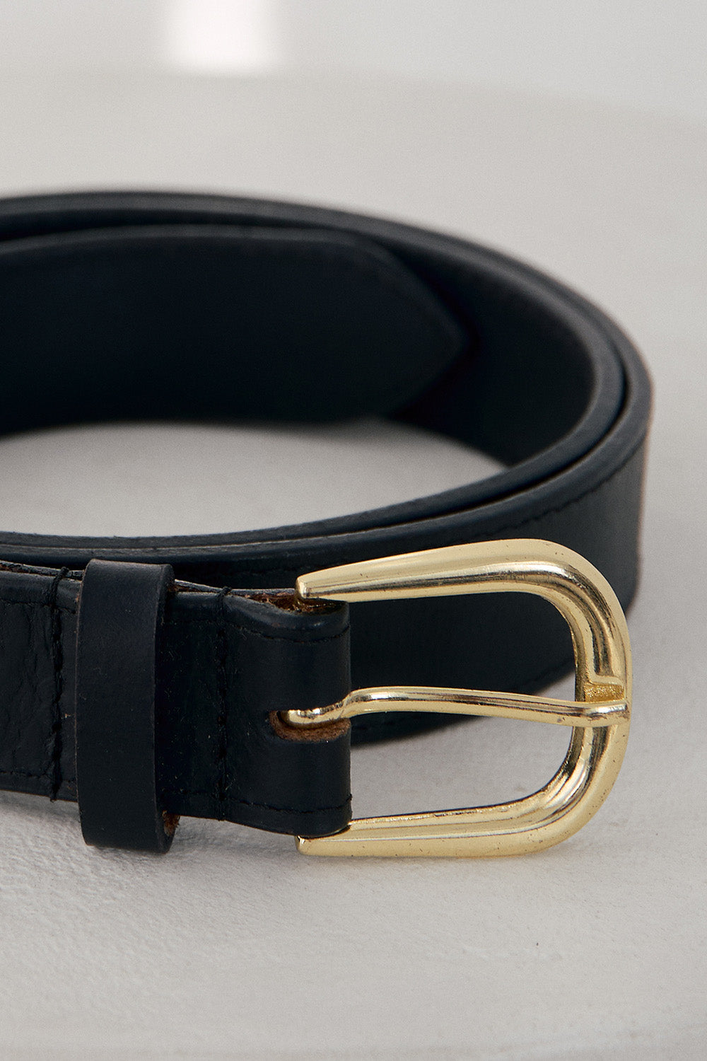 Black leather belt with a gold buckle on a light gray background