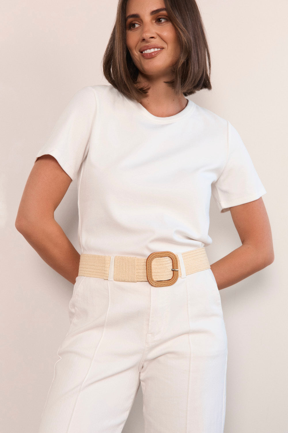 Woman wearing a white outfit with a beige belt against a plain background