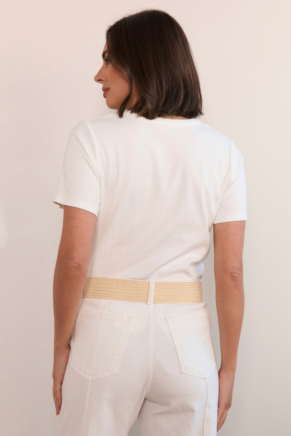 Woman wearing a white t-shirt and beige pants against a plain background