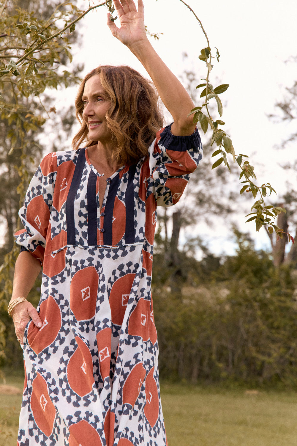 Woman in a patterned dress standing outdoors with trees in the background