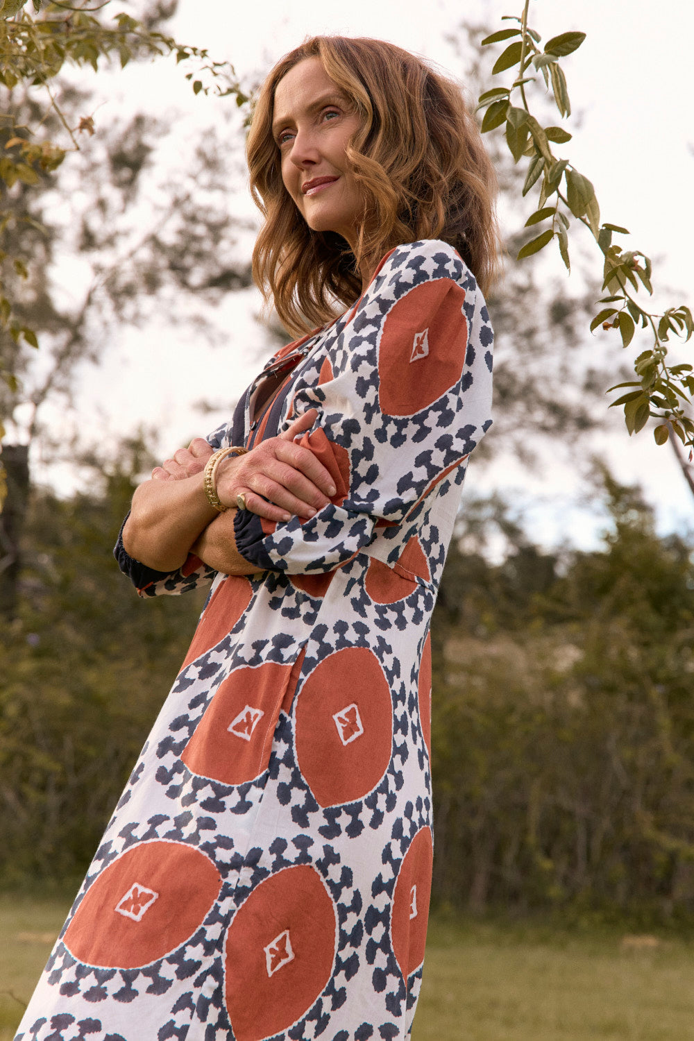 Woman wearing a patterned dress standing outdoors with trees in the background