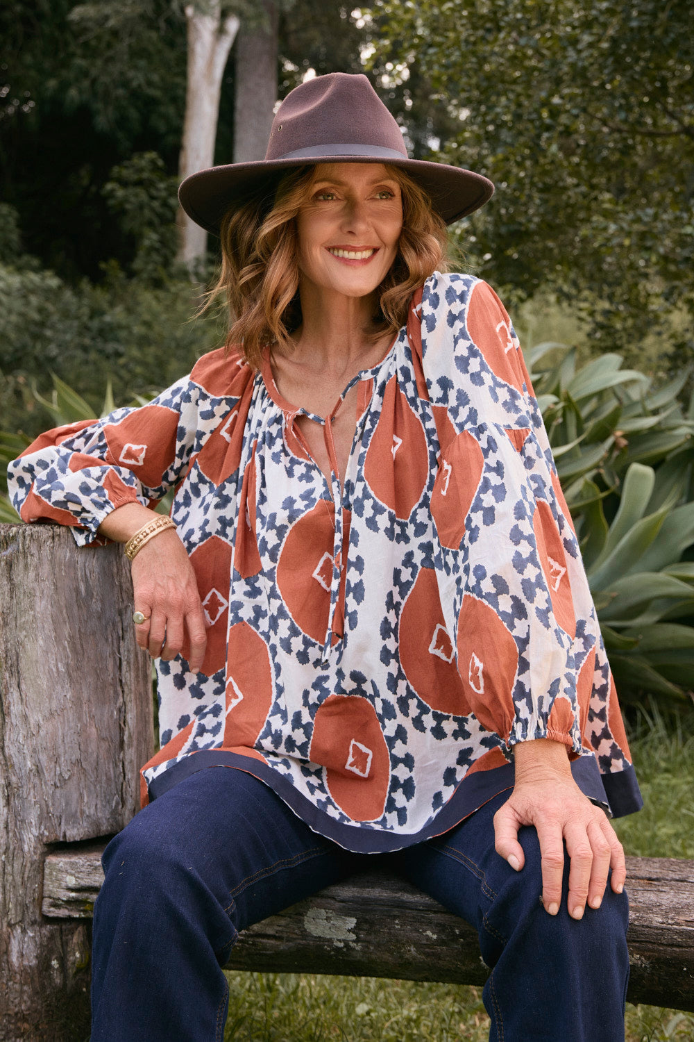 Woman sitting outdoors wearing a patterned blouse and hat