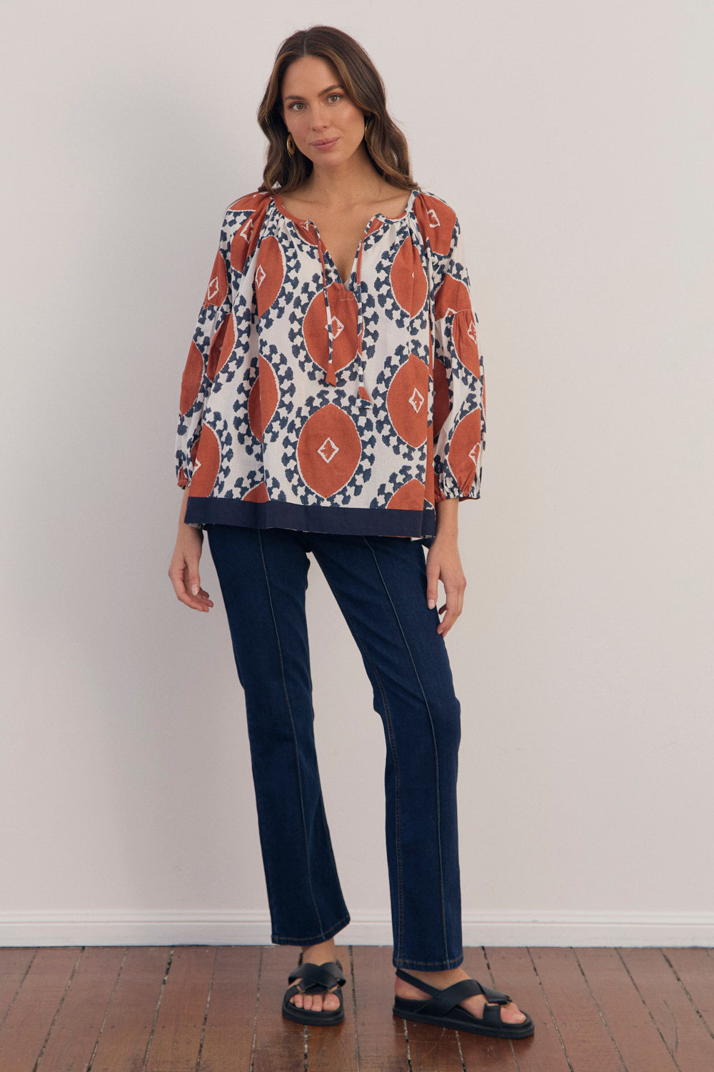 Woman wearing a patterned top and dark pants against a plain background