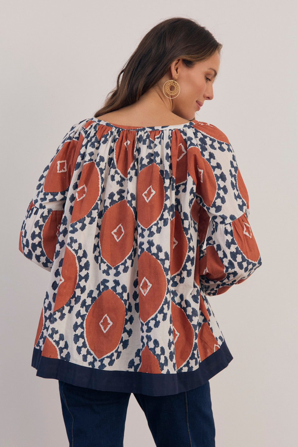 Woman wearing a patterned blouse with long sleeves on a plain background