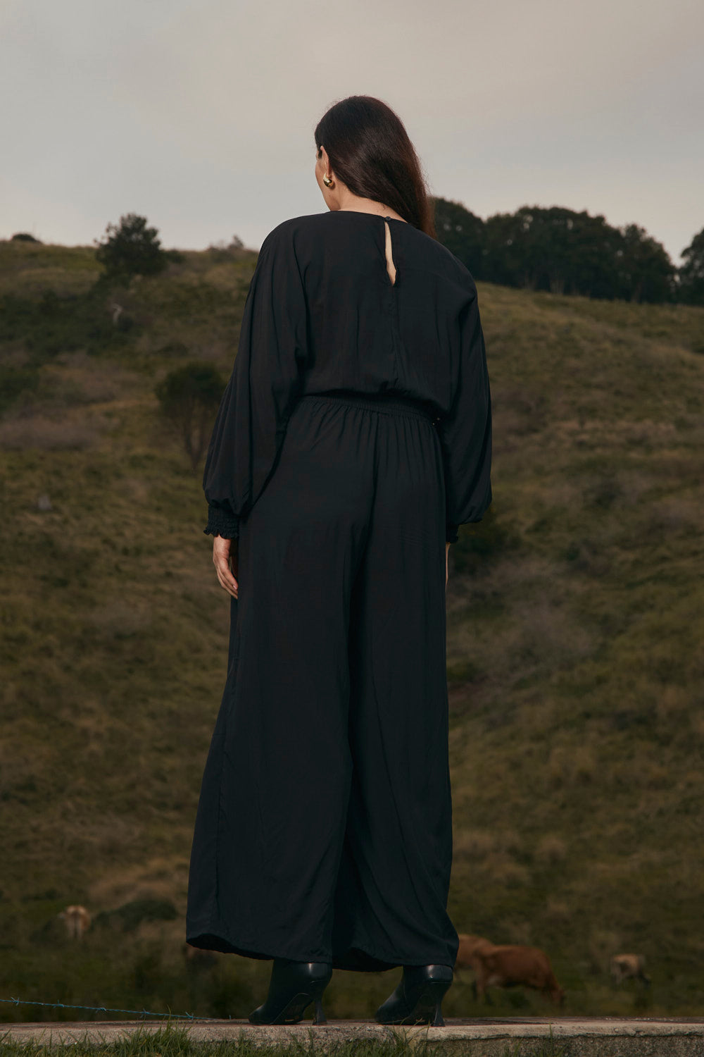 Person wearing a black outfit standing on a grassy hill with a scenic background
